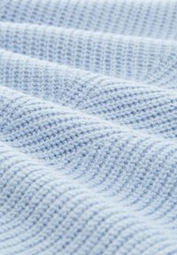 Lichtblauwe gebreide stof met een textuur en golvend patroon. Het materiaal is zacht en licht geribbeld, met gelijkmatige weefjes door het geheel.