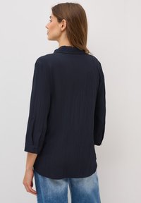 Marineblå, textured langærmet skjorte med båndkrave, knapmanchetter og afrundet kant, parret med lyseblå brede jeans.