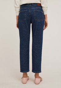 Vaqueros de mezclilla azul oscuro con corte recto, bolsillos traseros visibles y una parche de cuero marrón en la cintura. Se llevan zapatos rosas.