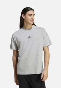 T-shirt grigio a maniche corte in cotone, con collo rotondo e un piccolo logo nero a tre righe sul petto.