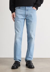 Heledad sinised teksad sirge säärega, viie tasku, lukuga ja kerge hõrenemisega. Kanda mustade libisevate kingadega.