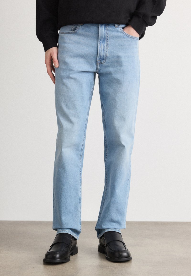 Heledad sinised teksad sirge säärega, viie tasku, lukuga ja kerge hõrenemisega. Kanda mustade libisevate kingadega.