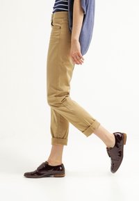 Khaki zúžené kalhoty s ohrnutými manžetami, zkombinované s tmavě burgundskými lakovými botami. Vrchní díl má modro-bílý pruhovaný design.