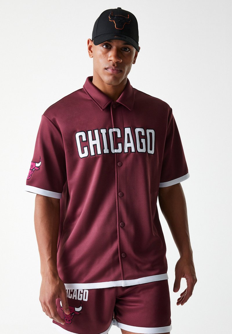 Bordo sportski dres s natpisom "CHICAGO" u bijelim slovima, kontrastne bijele pruge na rukavima, prikazan s odgovarajućim hlačama i crnim kapom.