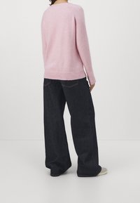 Rosa stickad tröja med ribbad nederkant, i kombination med lösa mörkblå jeans. Sedd bakifrån, vilket framhäver den mjuka texturen och den avslappnade designen.