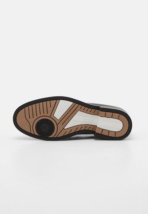 Semelle de chaussure noire avec bande de roulement marron et blanche, grip circulaire noir près de l'orteil, "BOSS" et "Made in Italy" embossés sur la semelle.