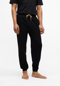 Crne trenirke od mekanog materijala, sa elastičnim pojasom i svetlom vezicom, suženim otvorima nogavica i bočnim džepovima.