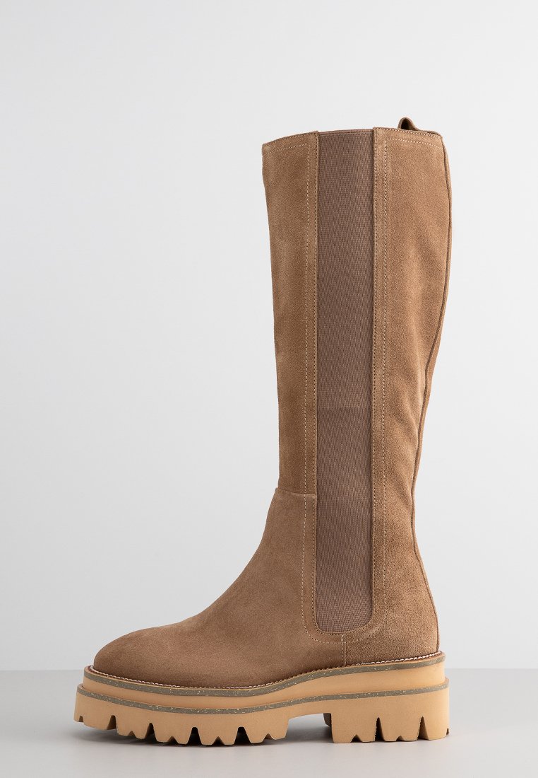 Schulterhohe, braune Wildlederstiefel mit einer strukturierten, elastischen Seitenpartie. Dicke, robuste Gummisohle mit einem leichten Plattformdesign.