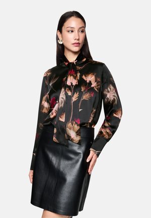 Floral-printed blouse in black satin with long sleeves and tie neck detail, paired with a fitted black leather skirt. Features soft texture.