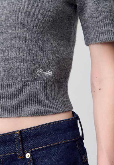 Maglione cropped grigio lavorato a maglia con orlo a coste. Presenta il logo ricamato "Claude". Abbinato a denim blu scuro, evidenzia la vita.