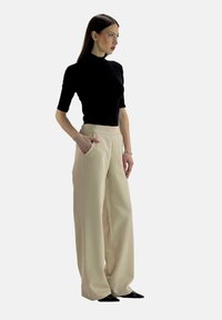Zwarte fitted top gecombineerd met beige wijde broek, voorzien van zijzakken en een gladde textuur, aangevuld met elegante zwarte schoenen.