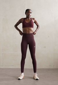 Bordå red sports-bh og høytlivs leggings laget av elastisk stoff, kombinert med lyse treningssko med svarte såler.