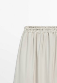Jupe beige clair avec taille élastique froncée, tissu lisse, vue de la taille vers le bas sur fond blanc.