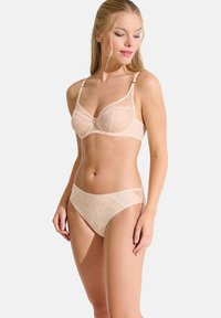 Ensemble de soutien-gorge en dentelle beige et culotte assortie. Le soutien-gorge présente un superposé de dentelle florale avec des bretelles ajustables et des détails de couture subtils.