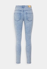 Jeans skinny azul claros com um efeito desbotado, cinco bolsos e um rótulo de couro na cintura. Apresenta um corte ajustado desde os quadris até os tornozelos.