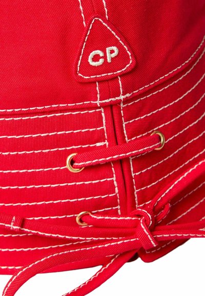 Cappello in cotone rosso con cuciture bianche, patch triangolare con logo "CP" e dettagli in oro, dotato di chiusura con cordino per una vestibilità sicura.