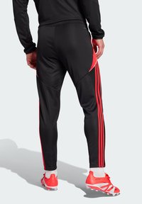 Zwarte sportbroek met rode zijaccenten en strepen; gemaakt van gladde, flexibele stof met een tapered fit.