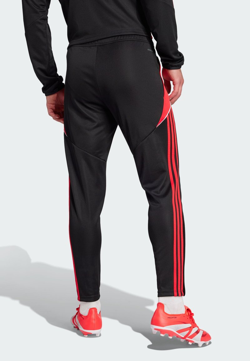 Pantalons de sport noirs avec des accents et des rayures rouges sur les côtés ; fabriqués à partir d'un tissu lisse et flexible avec une coupe ajustée.