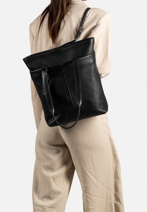 Zwarte leren tote bag met een gestructureerde afwerking, voorzien van lange handgrepen en een ritsluiting, gepositioneerd tegen een neutrale achtergrond.