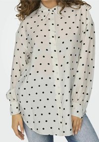 White long-sleeve shirt with black polka dots, button-front, collar, and gathered cuffs. Fabric appears lightweight and slightly sheer.