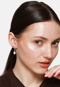 Boucles d'oreilles pendantes avec un métal argent�é et des pierres rondes opalescentes. Le design est rehaussé d'une délicate chaîne.