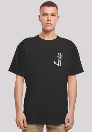 Black cotton T-shirt with short sleeves, featuring white text and an anchor graphic on the left side. Casual, loose-fit design.