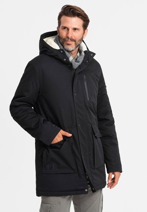 Parka negra aislada con capucha, bolsillo en el pecho con cremallera y bolsillos delanteros con botón. Cuenta con un acogedor forro de piel sintética.