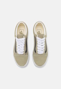 Beige suede sneakers with white laces, black side accents, and a cream interior featuring a logo on the insole. Low-cut design.