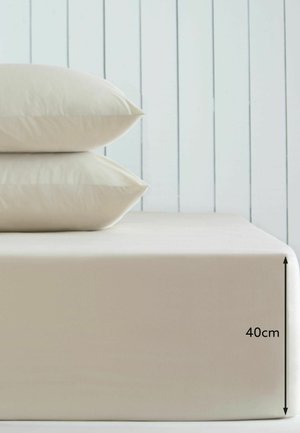 Zwei gestapelte beige Kissen auf einer beigen Matratze mit 40 cm Dicke vor einer hellen Holzpaneelwand.