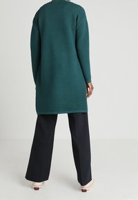 Teal ribbad klänning med långa ärmar, rund hals och lös passform, kombinerad med vida svarta byxor och vita skor.