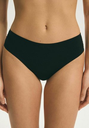Kobieta nosząca proste czarne majtki w stylu bikini, pokazująca talię, biodra i górną część ud na jednolitym tle.