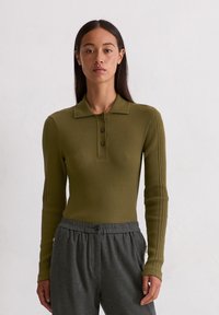 Olijfgroen geribd longsleeve polo shirt met een kraag en drie knopen, gecombineerd met grijze broek met elastische tailleband en een zijzak.