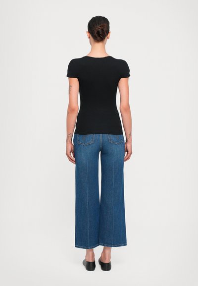 Svart tajt T-shirt med kort ärm, matchad med vida blå jeans i denim. Jeansens design har hög midja och bakfickor. Enkelt och rent utseende.