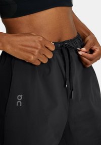 Svarta träningsshorts med elastisk midja och dragsko. Har en slät yta och en logotyp på nedre vänstra sidan.