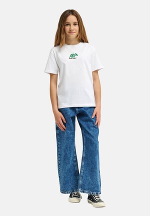 Biała bawełniana koszulka z zielonym graficznym logo na piersi, zestawiona z szerokimi niebieskimi dżinsami i czarnymi tenisówkami.