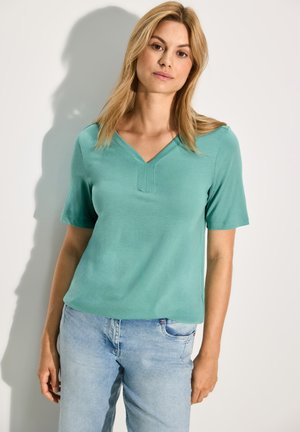 Haut turquoise à manches courtes avec un col en V et des détails de couture subtils. Associé à un jean bleu clair, au tissu lisse et à la coupe décontractée.