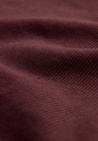 Burgunderstoff hat eine strukturierte, gerippte Oberfläche mit feinen Linien. Das Material wirkt weich und flexibel, mit einer reichen, tiefen Farbe.