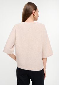 Helles Rosa, kurzärmliger Pullover mit rundem Ausschnitt, weichem Material und leicht verkürztem Schnitt, von hinten vor einem weißen Hintergrund gezeigt.