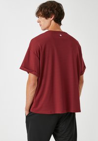 Camisa de manga corta color marrón con un corte relajado, textura acanalada y mangas enrolladas. Presenta un pequeño logo en la parte posterior del cuello.