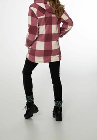 Felpa in pile a fantasia tartan crema e bordeaux, con cappuccio, abbinata a leggings neri e sneakers nere con calzini a stampa leopardata verde.