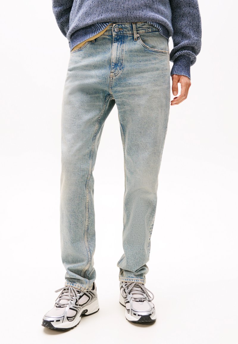 Lichtblauwe denim jeans met een rechte pasvorm, vervaagde textuur, vijf zakken en een standaard knoopsluiting, gecombineerd met wit- en zwartgekleurde sneakers.