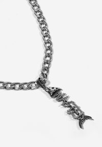 Collar de cadena en tono plateado que presenta un colgante en forma de espina de pescado con detalles intrincados y un acabado pulido, que enfatiza texturas y formas.