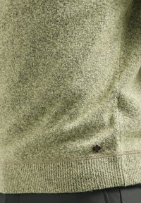 Groen gestructureerd vest met een geribbelde zoom en logo-accent. De stof heeft een zachte uitstraling met een gemêleerd patroon.