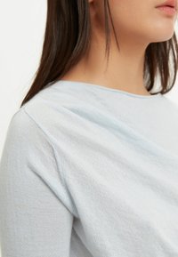 Hellblaues Baumwolloberteil mit weicher Textur, rundem Halsausschnitt und abfallenden Schulternähten. Nahaufnahme zeigt die Webart des Stoffes.