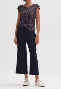 Top navy con scollatura rotonda e maniche corte, con un motivo a pois multicolore; abbinato a pantaloni larghi scuri e sneakers bianche.