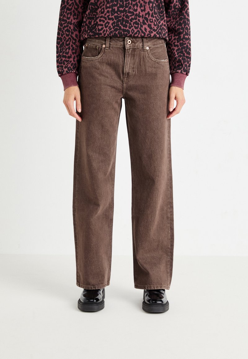 Barna, bővített lábú farmernadrág, gombos záródással, öt zsebbel és finom fakulással. Fekete cipővel párosítva.