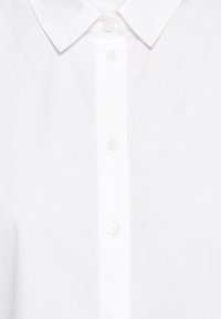 Chemise blanche à boutons avec un col classique, une patte de boutonnage à l'avant et une texture de tissu lisse et légère.