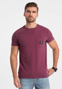 Korte ærmer, rundhals T-shirt i en dyb maroon farve, med en venstre brystlomme med et karakteristisk sort mærke. Blød stoftekstur.