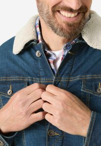 Denim jacket with a cream sherpa collar, chest pockets, metal button closures, and yellow stitching details. Visible plaid shirt underneath.