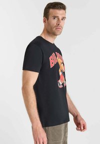 Camiseta de algodón negra con un estampado gráfico de un oso en indumentaria deportiva, con acentos en rojo y blanco y mangas cortas.